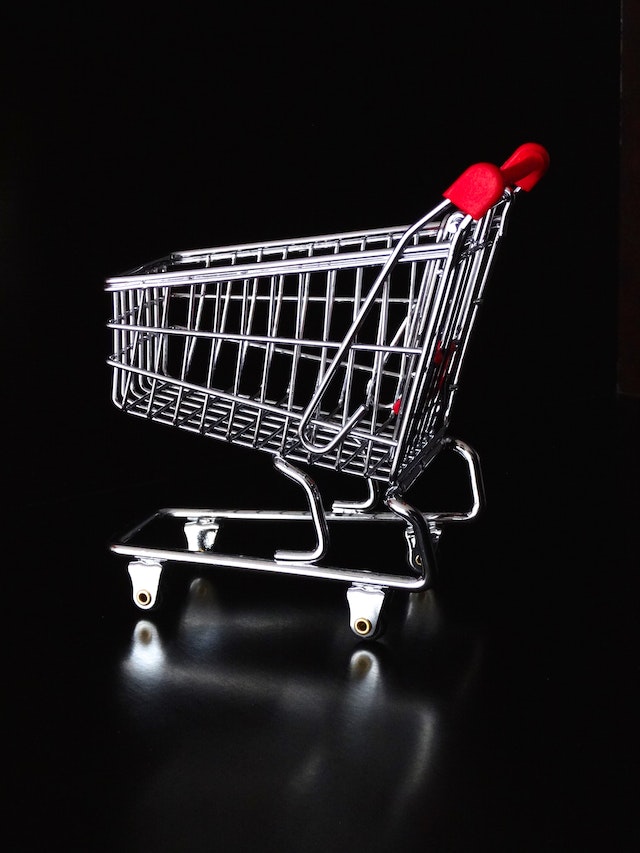 metal shopping cart with red handle on a black background